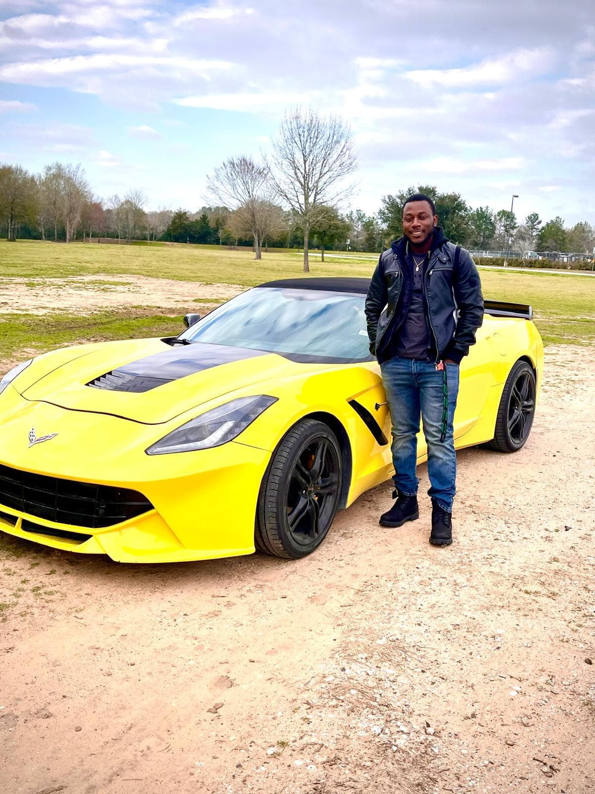 Desmond Lamptey standing beside a yellow sports car outdoors.